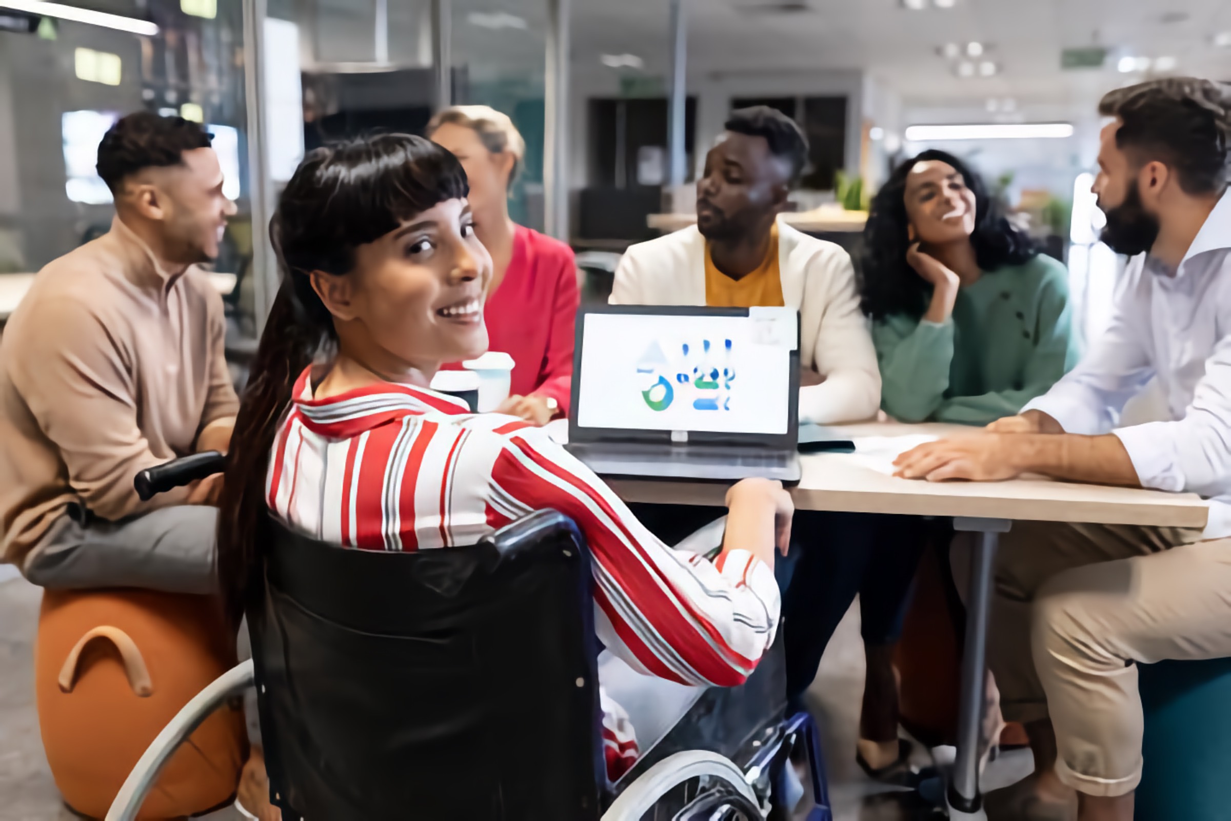 Diverse group meeting including a smiling biracial woman who uses a wheelchair