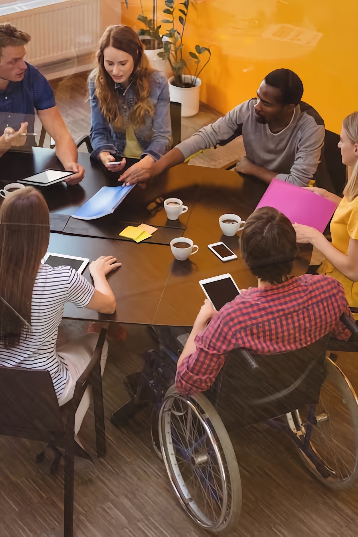 Meeting of people sitting around a table from different genders, races, and People with Disabilities