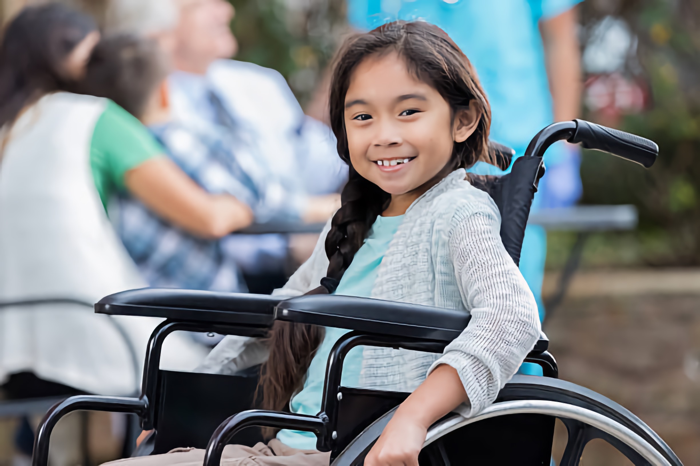 Smiling young girl using a wheelchair enjoying a diverse outdoor community event
