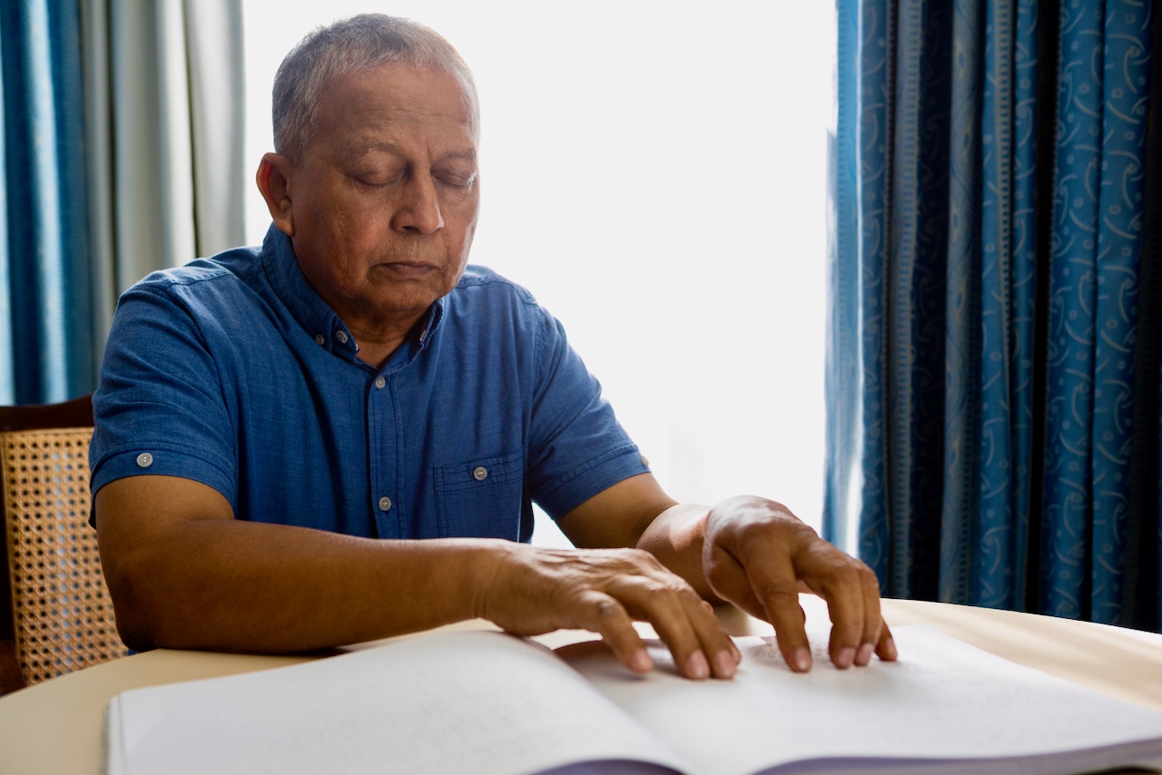 An older man sitting at a table, reading a Braille book