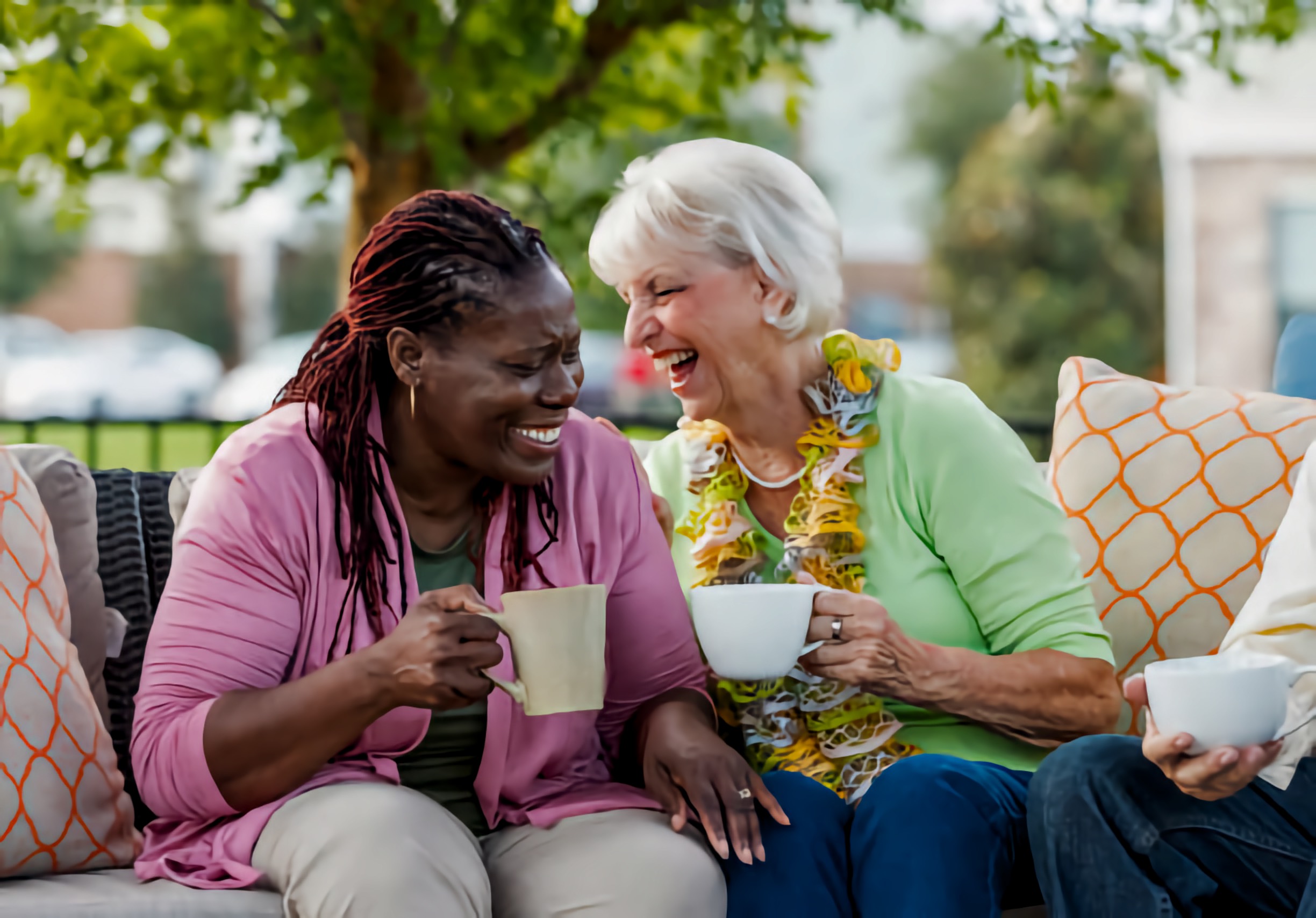 Two older women, one Black and one white, sharing laughs and coffee outside