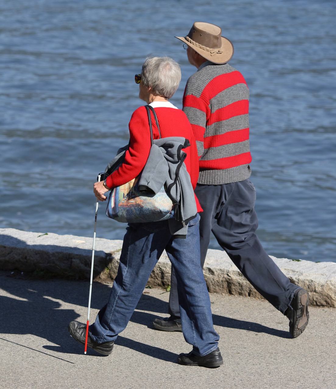 An outdoor scene with an older couple where the woman is Blind and using her white cane out for a walk in the fresh air and sunshine