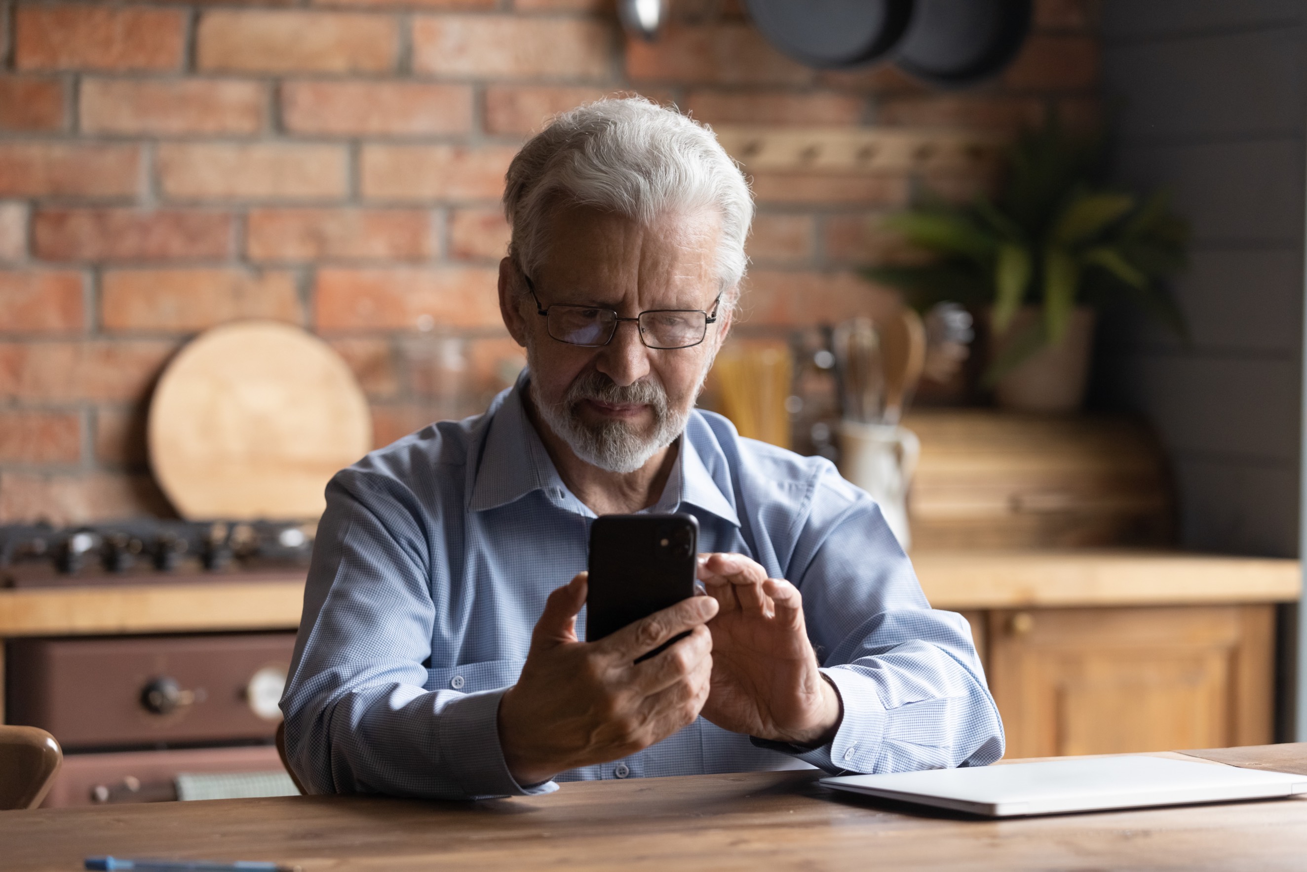 Older man wearing glasses uses his mobile phone to look up information