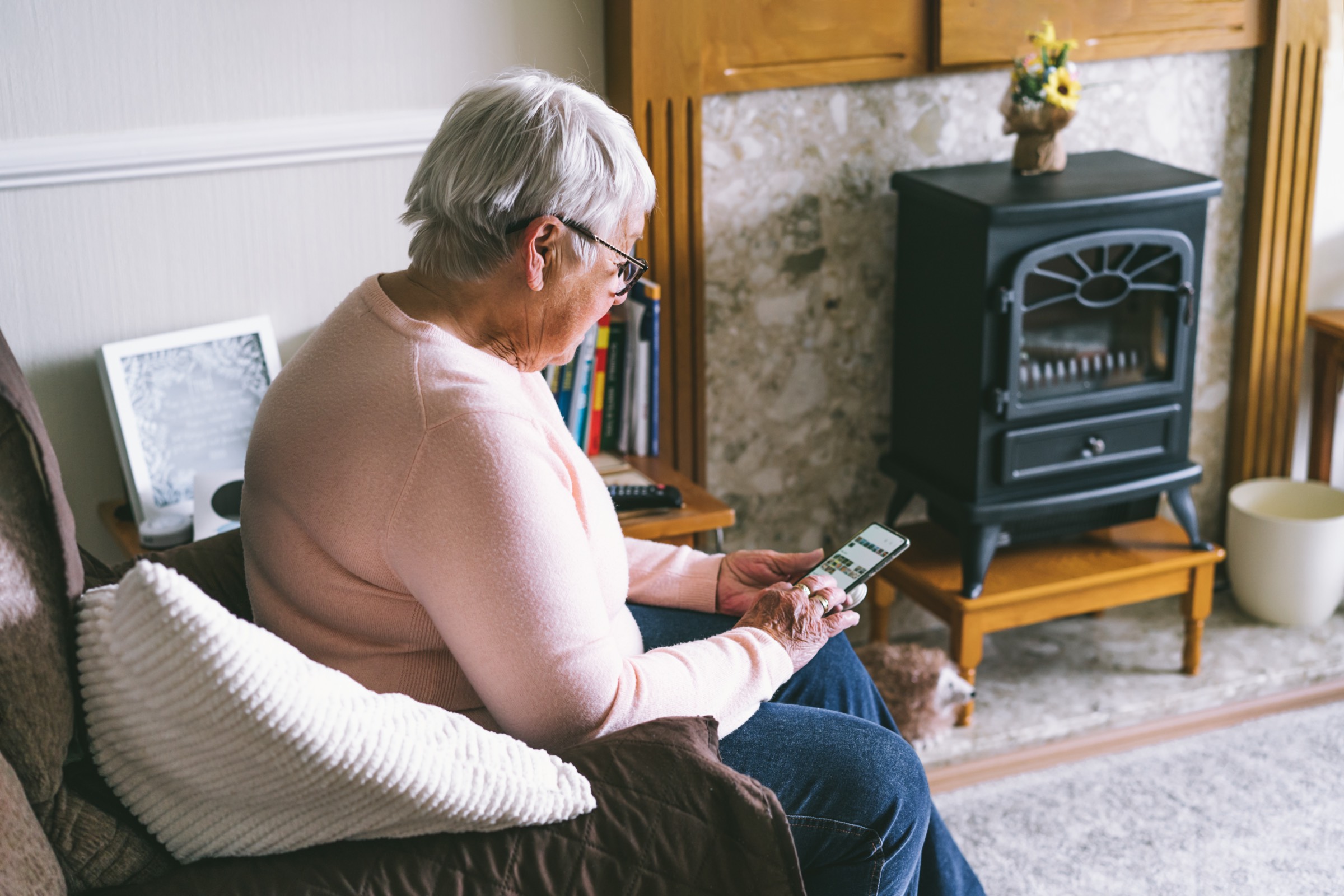 Older woman using smartphone to access information online while sitting on an armchair at home