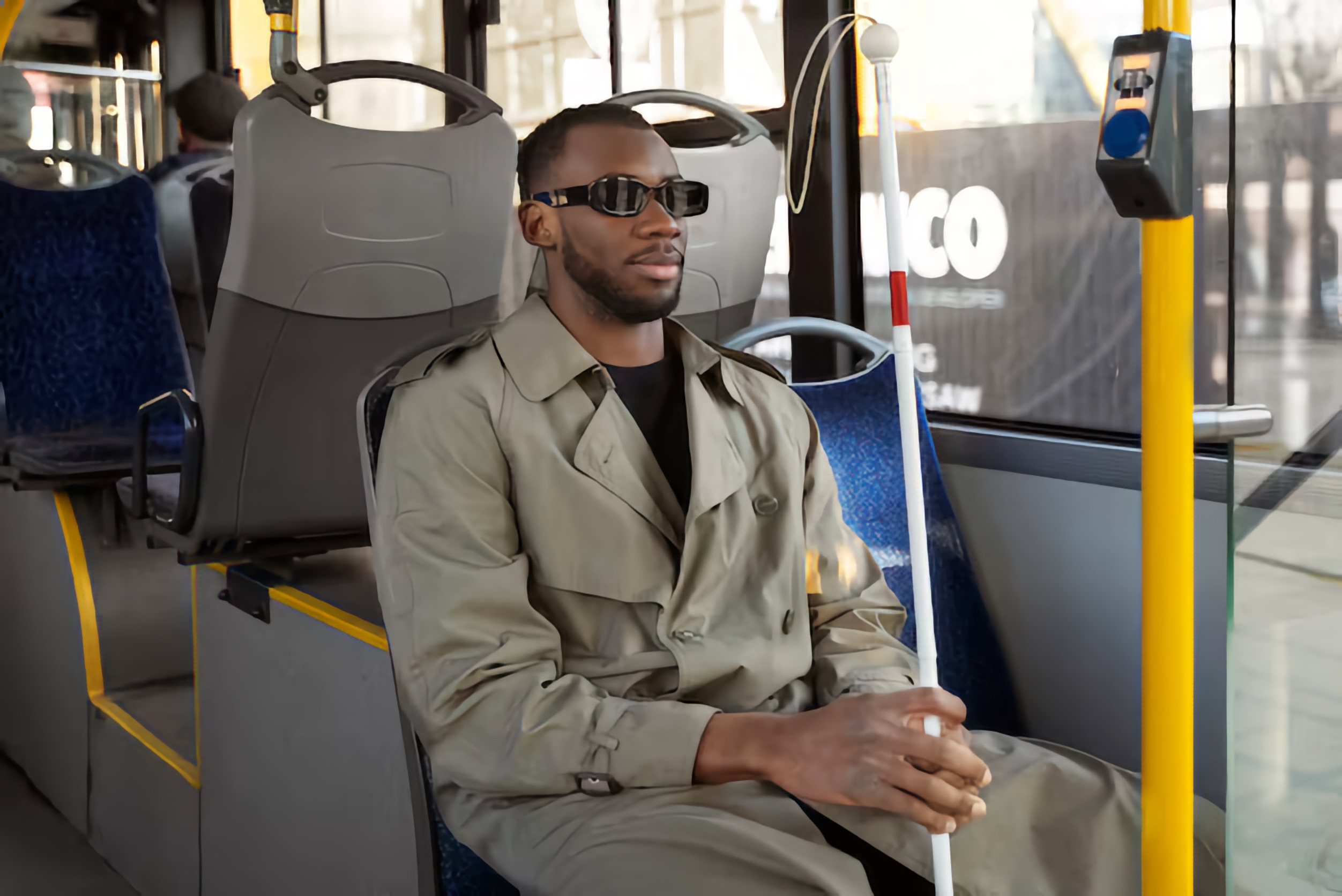 A Black man who is Blind sits comfortably on a bus seat, holding a white cane.