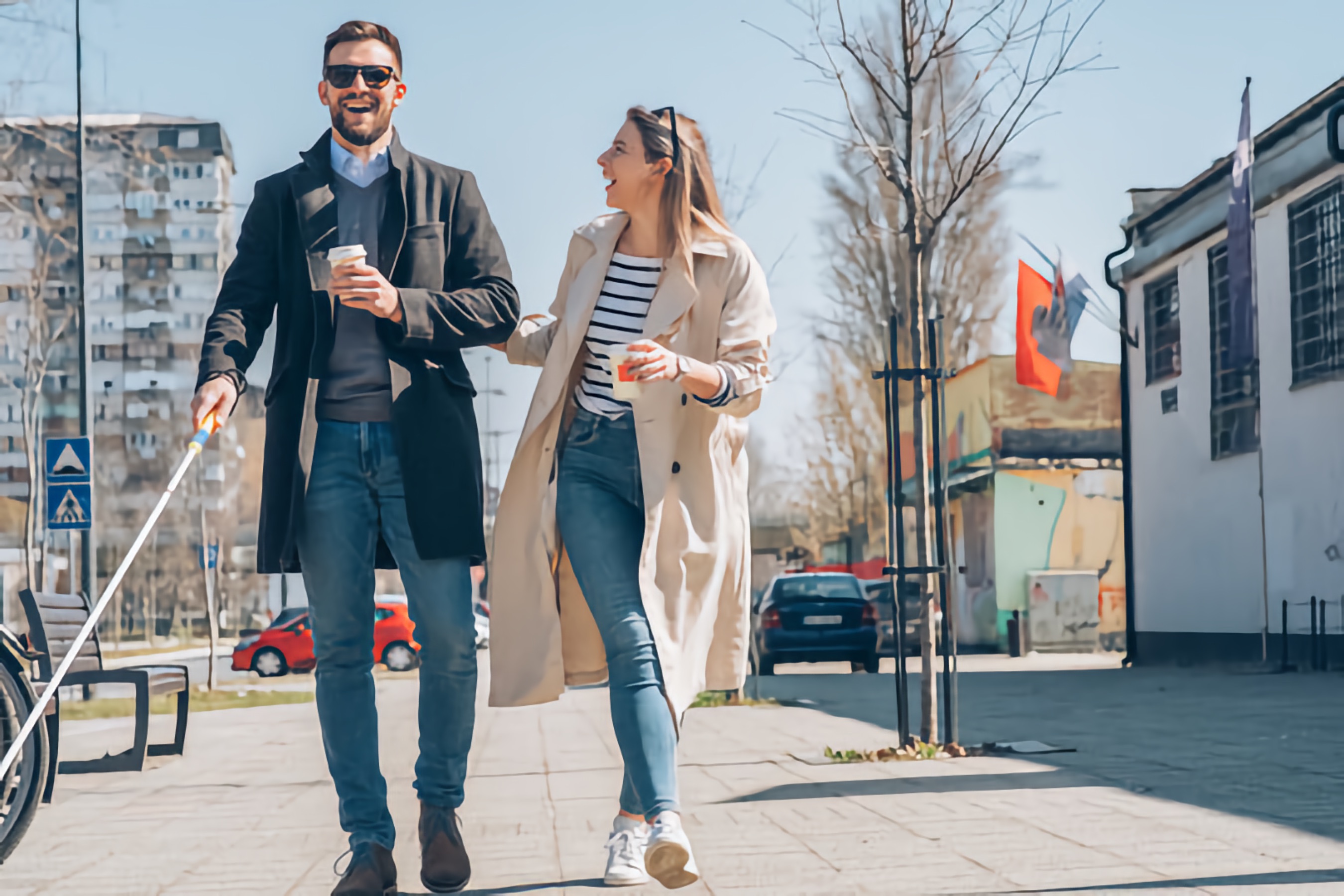 A Blind man with a white cane and a woman walk arm in arm, both smiling. Colorful buildings and parked cars are in the background.
