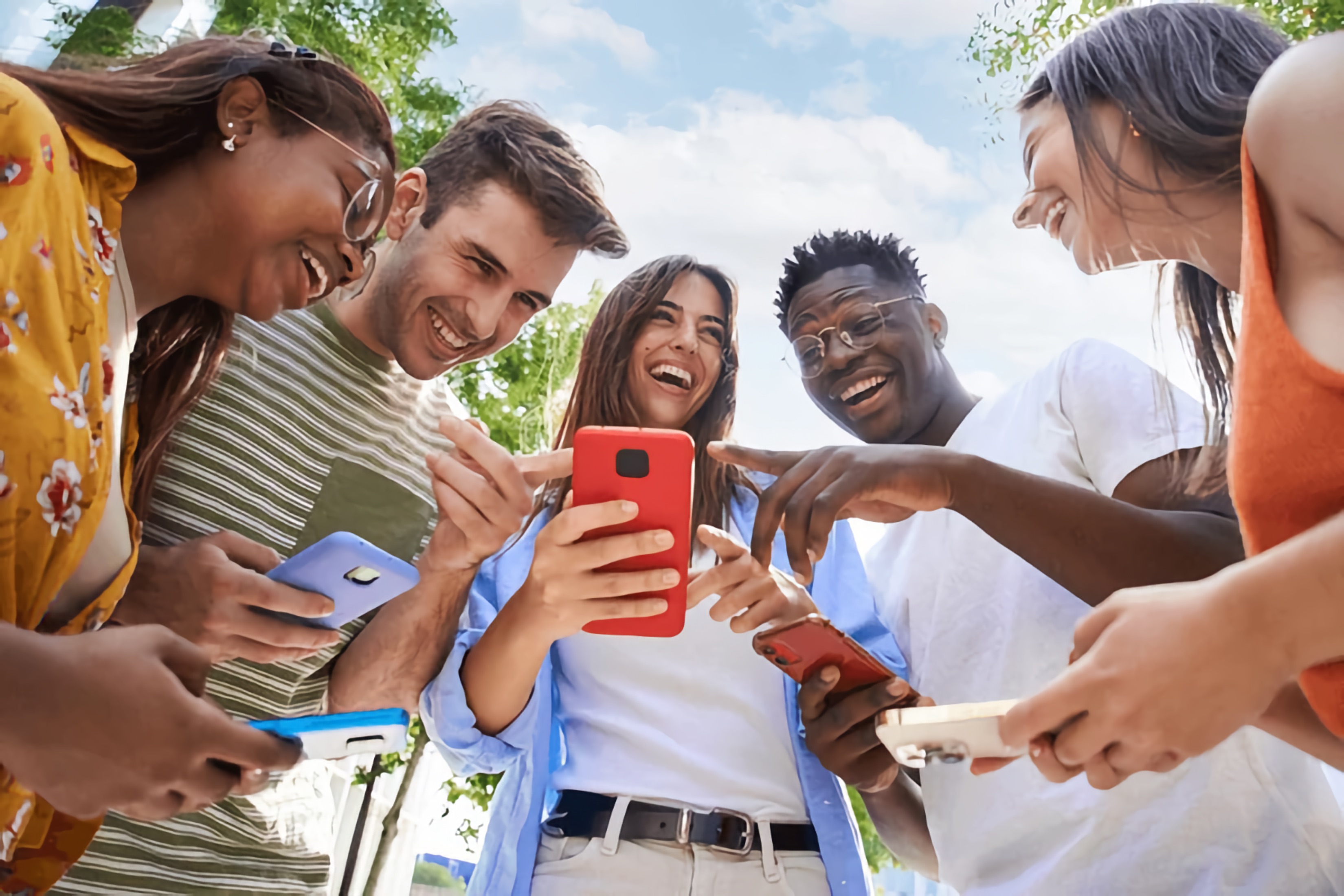 A diverse group of young people laughing and sharing information on their mobile phones.