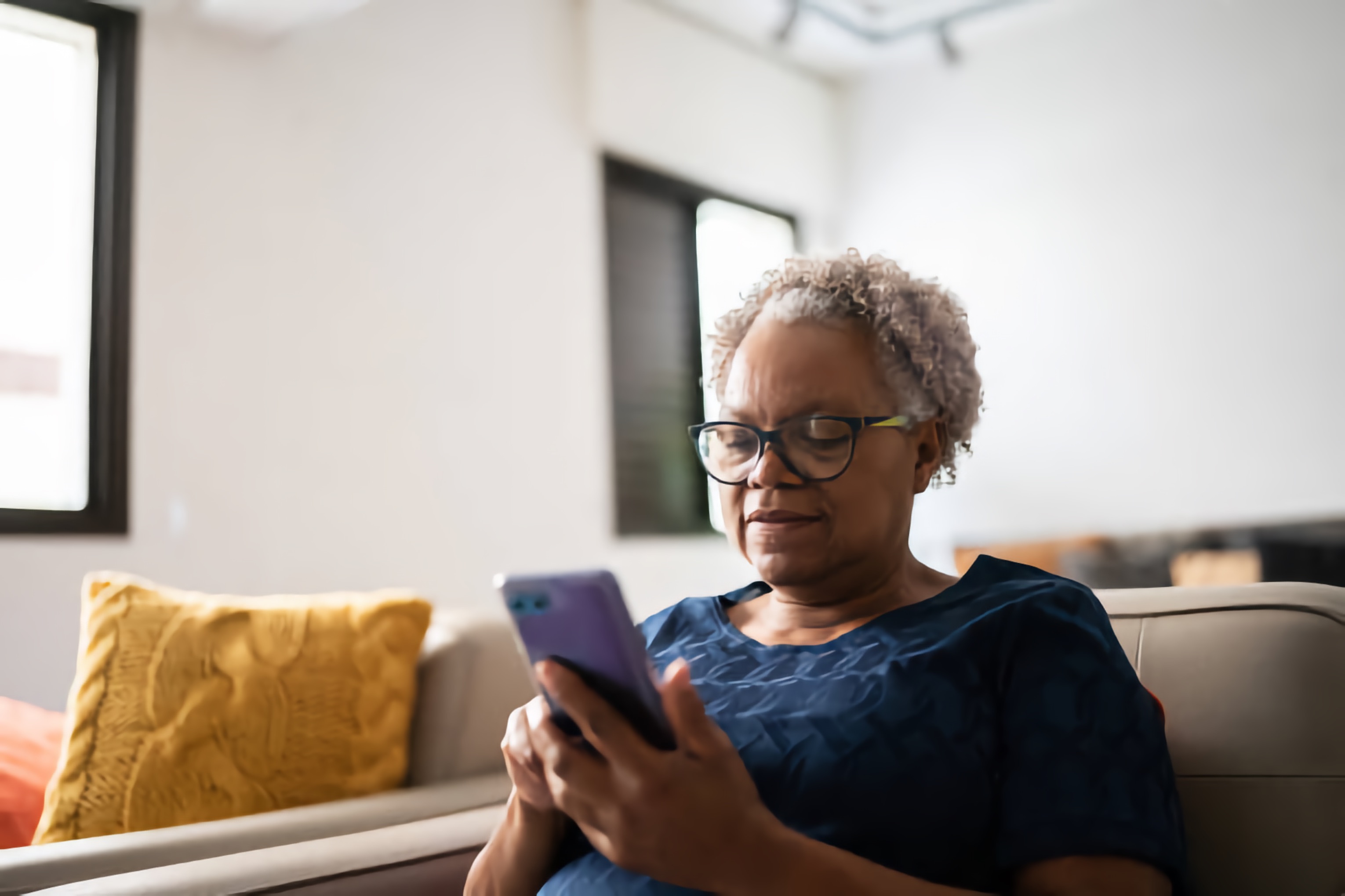 An older Black woman reads information on her smartphone in her living room.