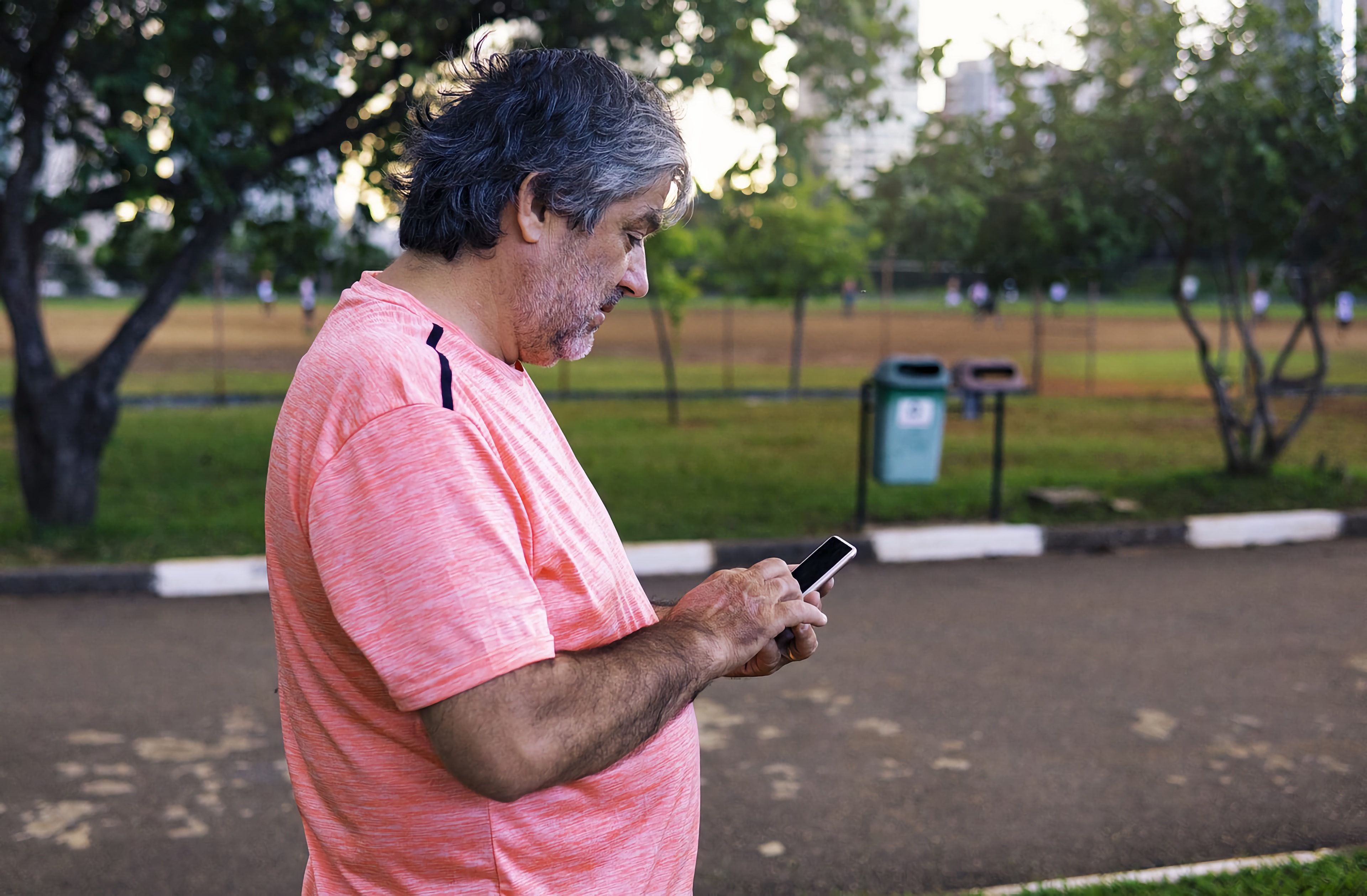 An older man in an outdoor setting accesses information on his smartphone.