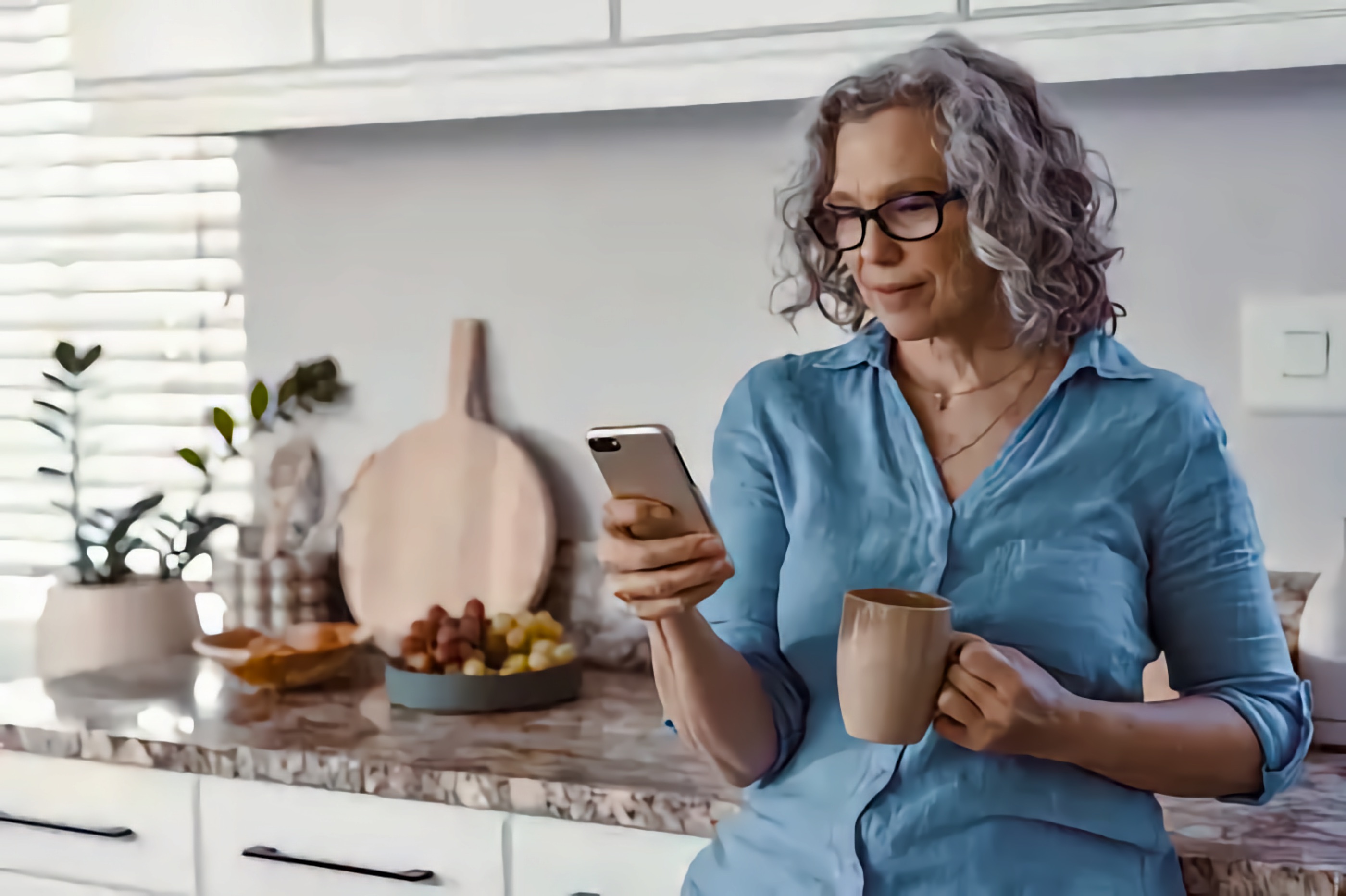 An older woman in her kitchen looks at information on her smartphone.