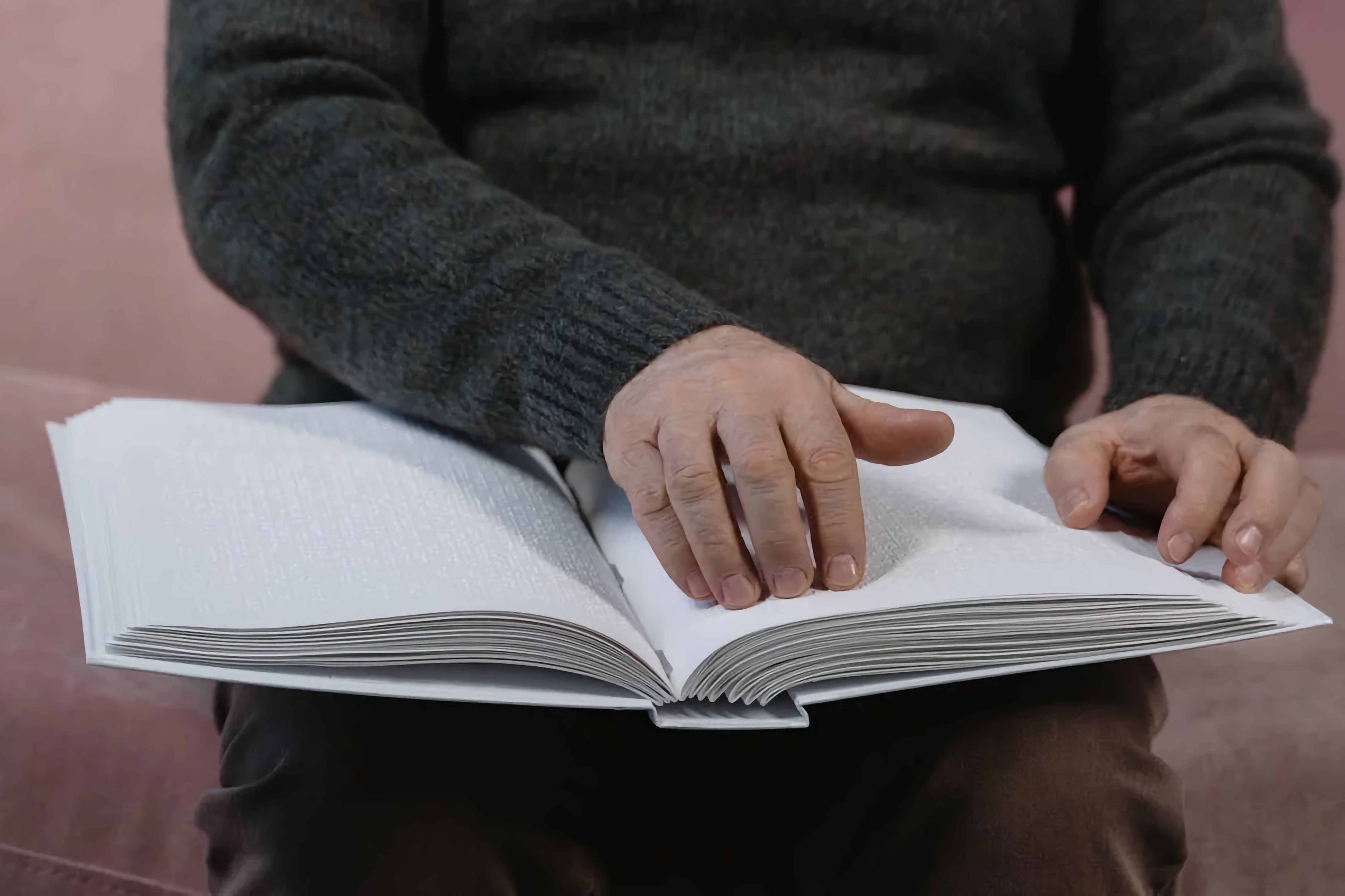 Close-up image showing the hands of an older Blind man reading a Braille book