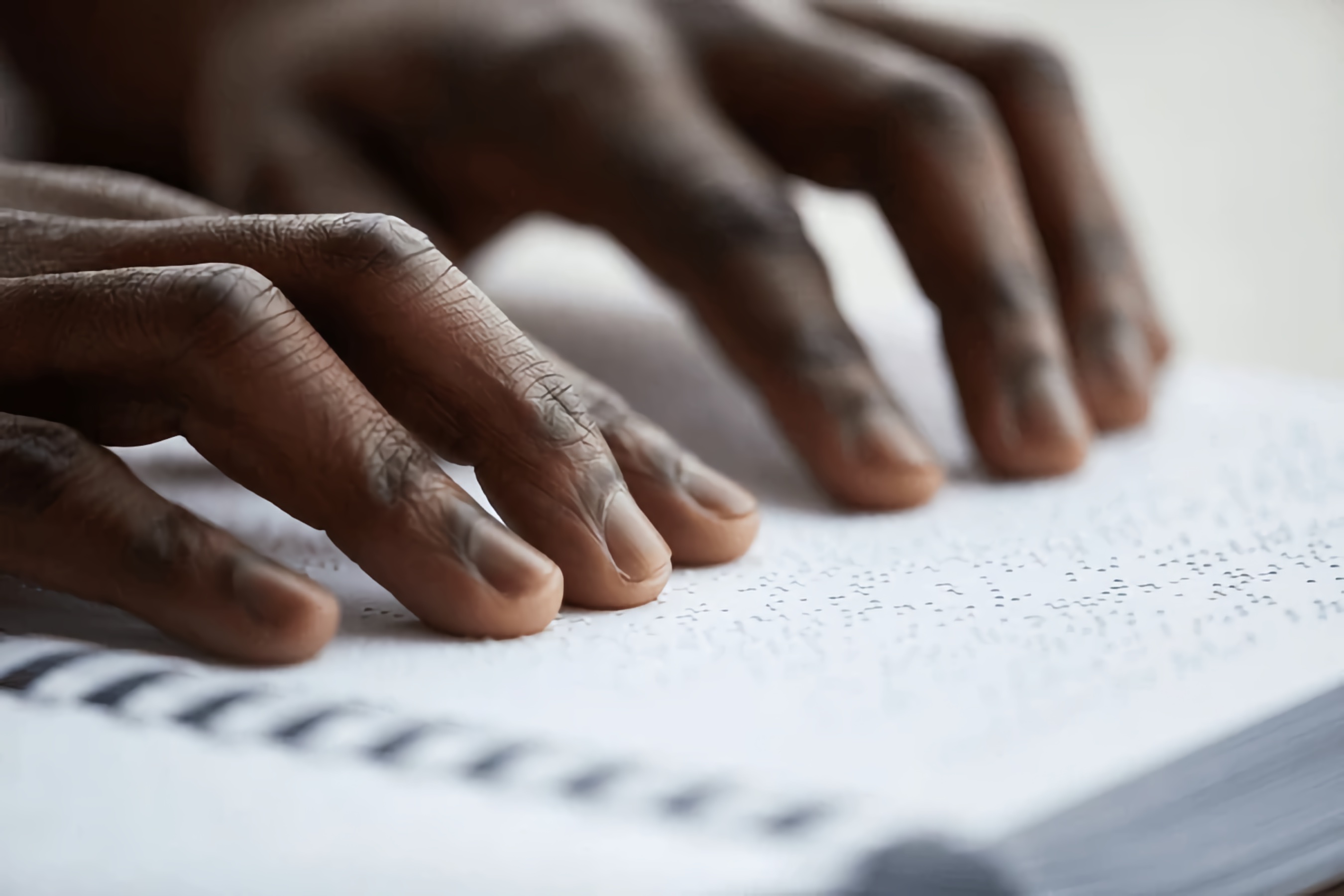 Close-up of the hands of a Blind Black man reading a Braille book