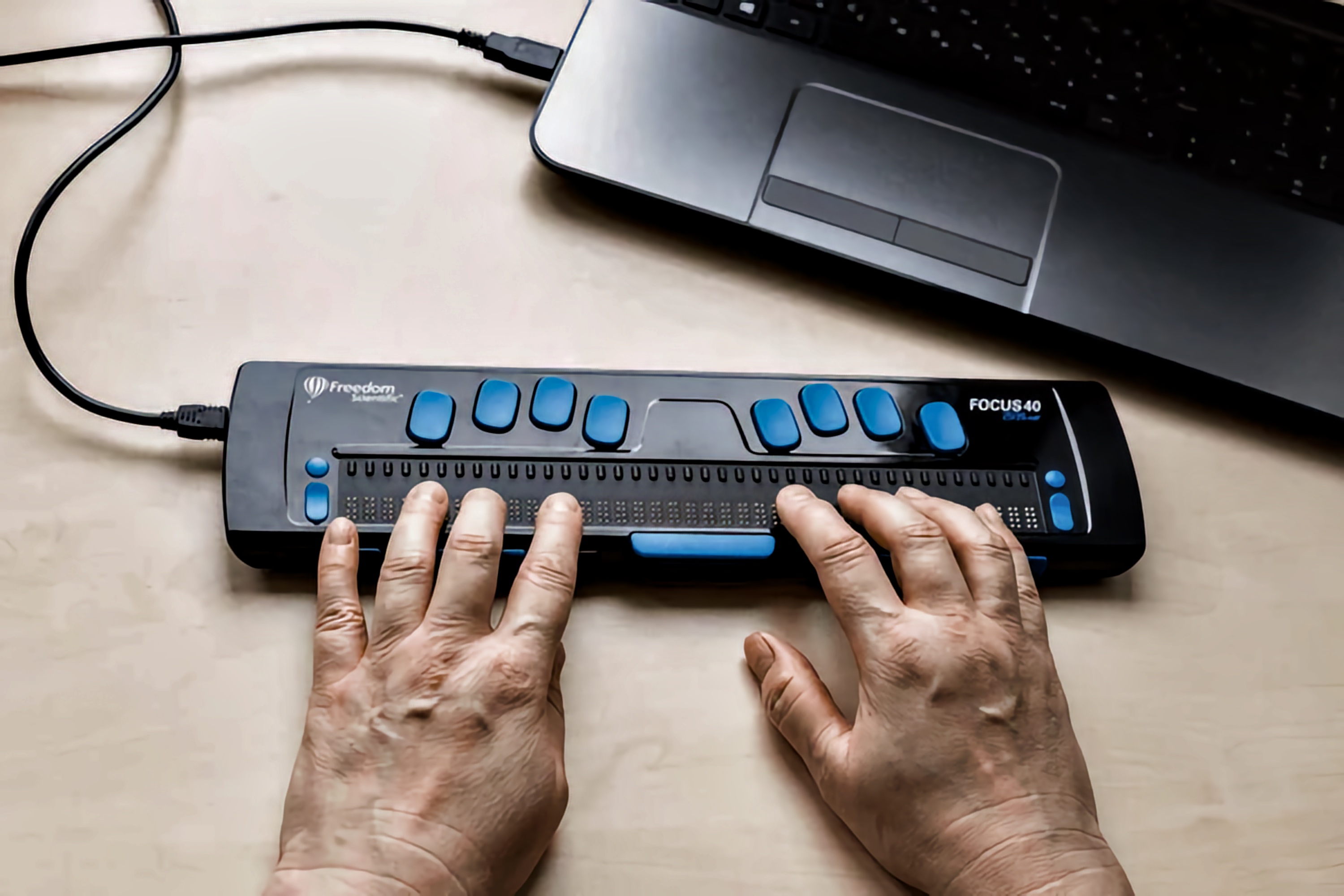 Hands gliding over the raised Braille cells of a Focus 40 Braille Display, accessing Accessible Information.