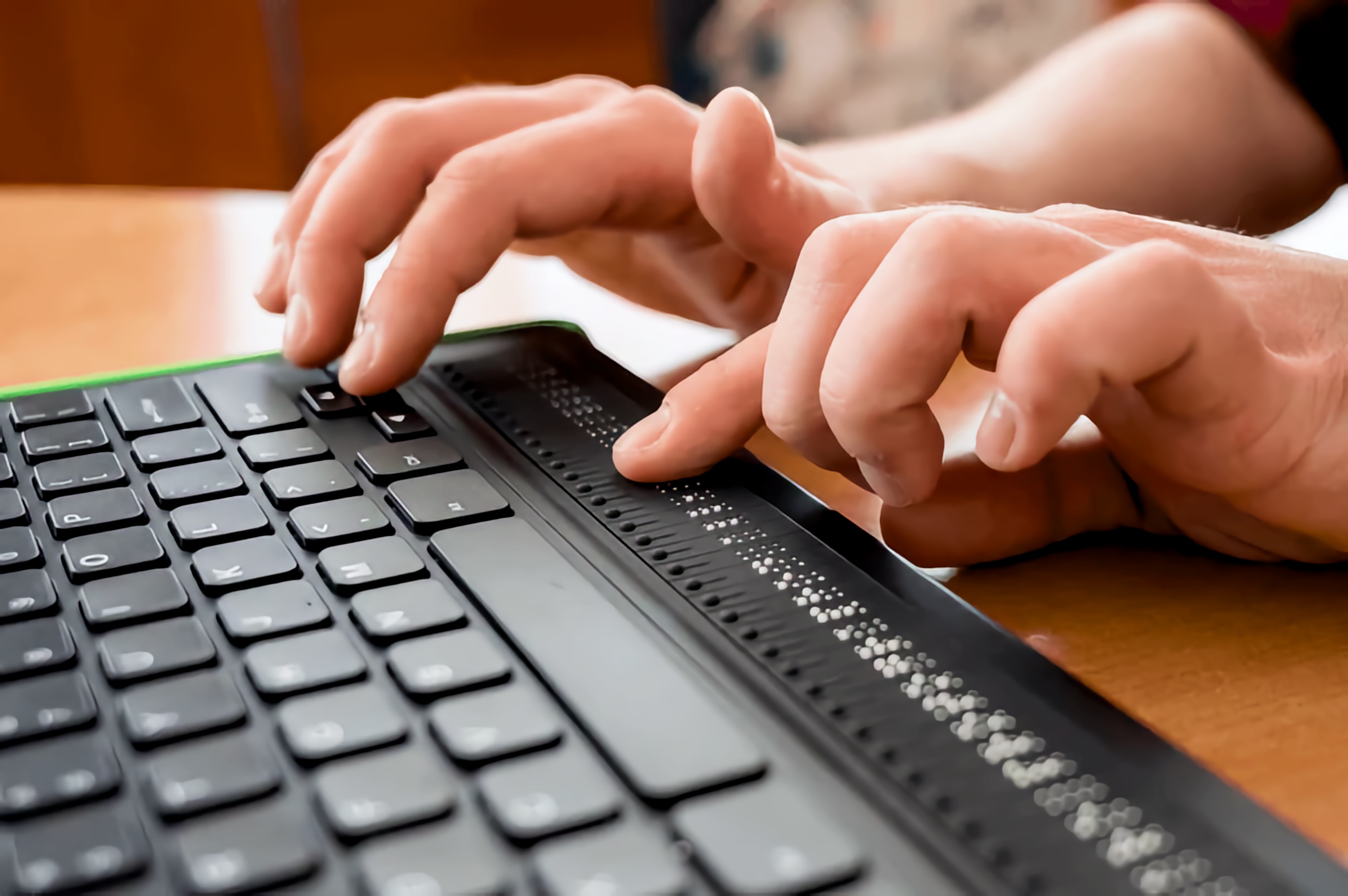 Close-up of hands typing on a keyboard that includes a Refreshable Braille Display, allowing tactile access to digital text.
