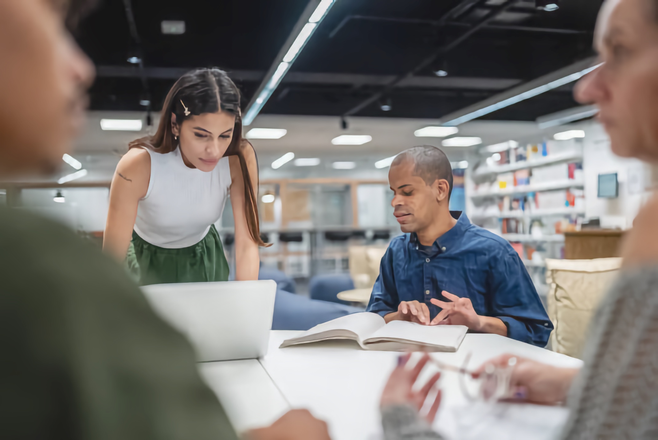 A small study group collaborates around a table while one person reads a Braille book and another reviews notes on a laptop.