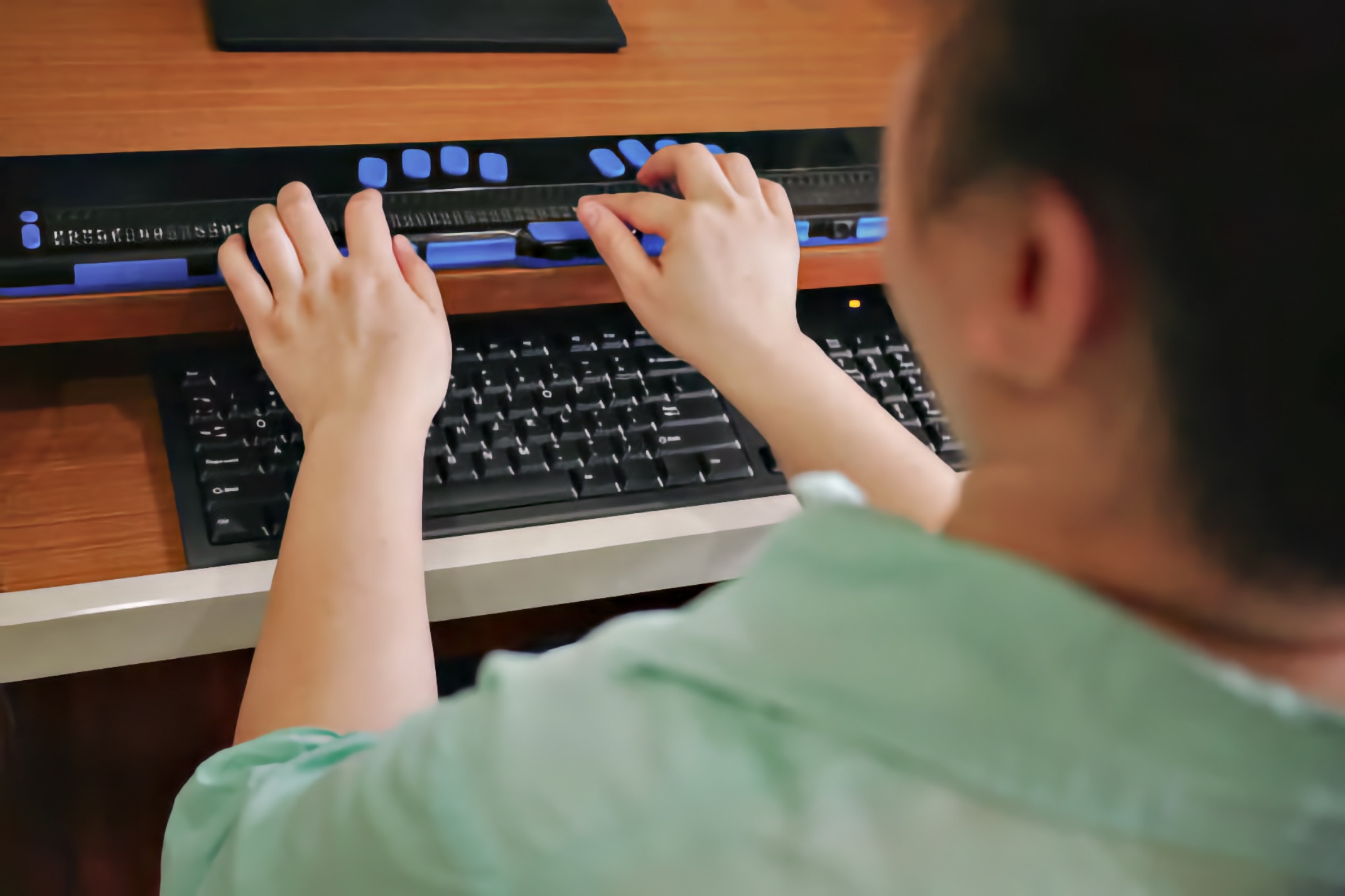 Person using a refreshable braille display above a computer keyboard at a desk