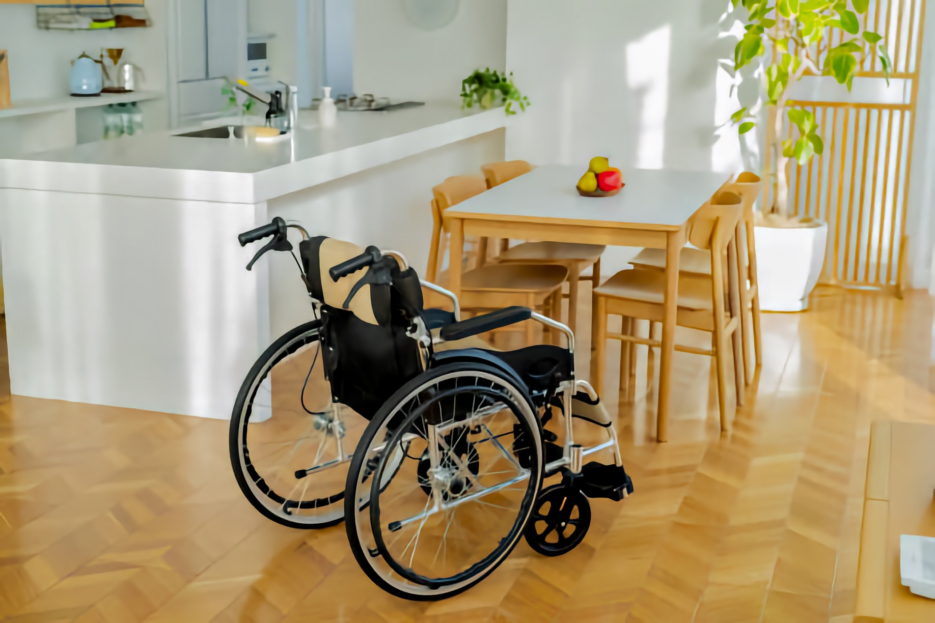 Manual wheelchair near a wooden dining table on a parquet floor; houseplants and wide passageways suggest a step-free layout designed for everyday living.