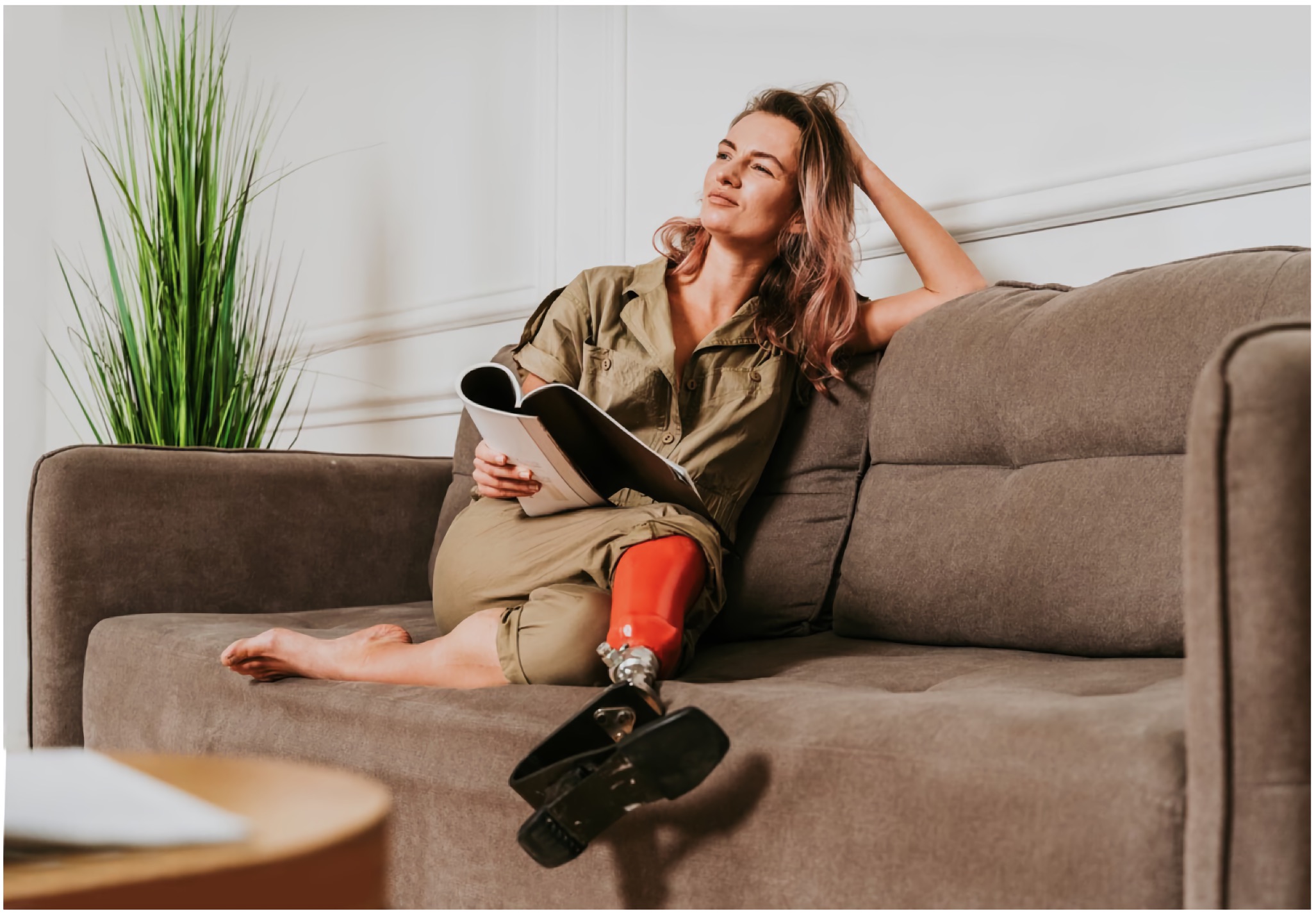 Woman with a prosthetic leg relaxing on a hotel sofa, notebook in hand, looking reflective.