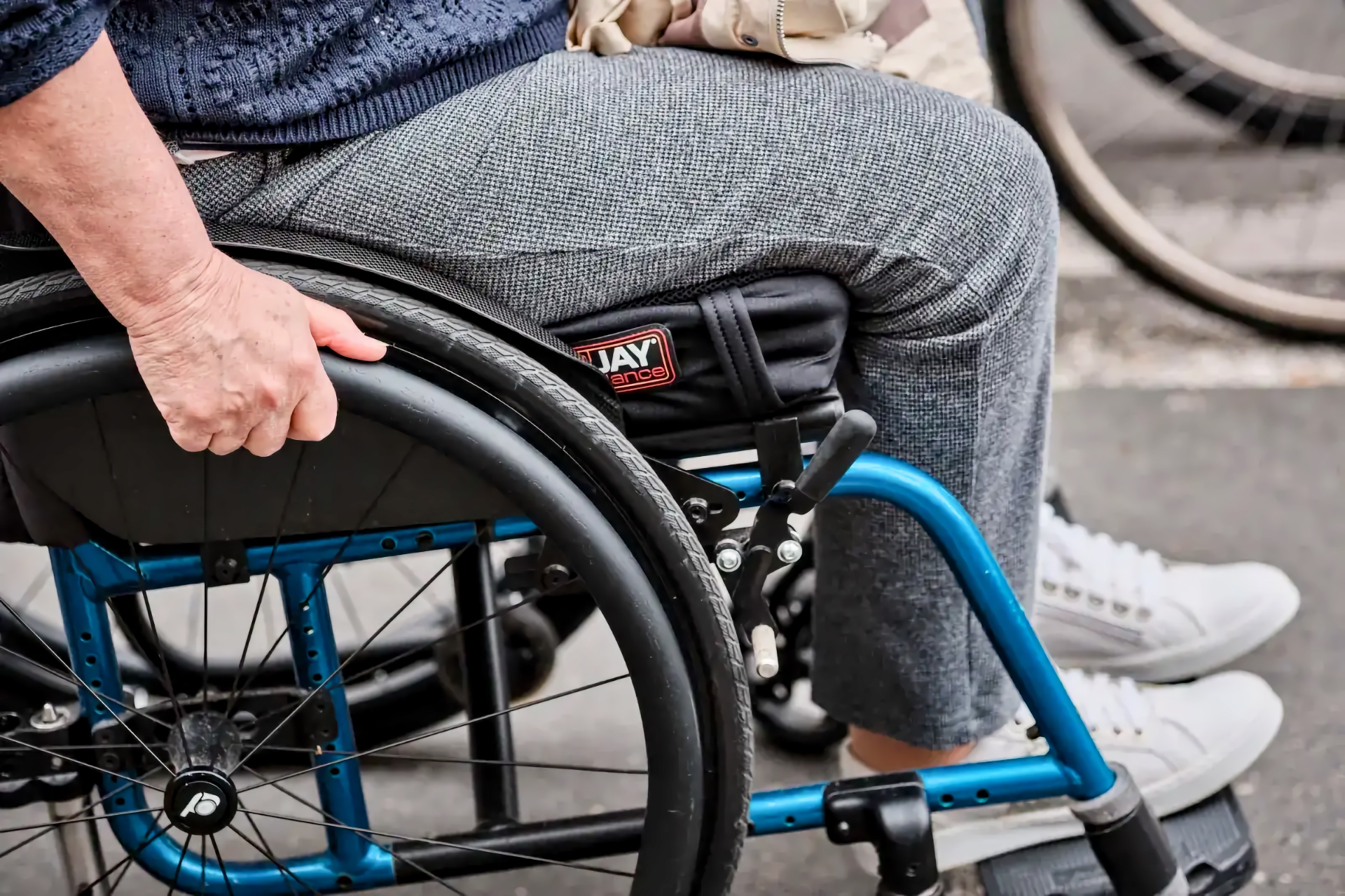 Older adult in a blue-framed manual wheelchair gripping the push rim.