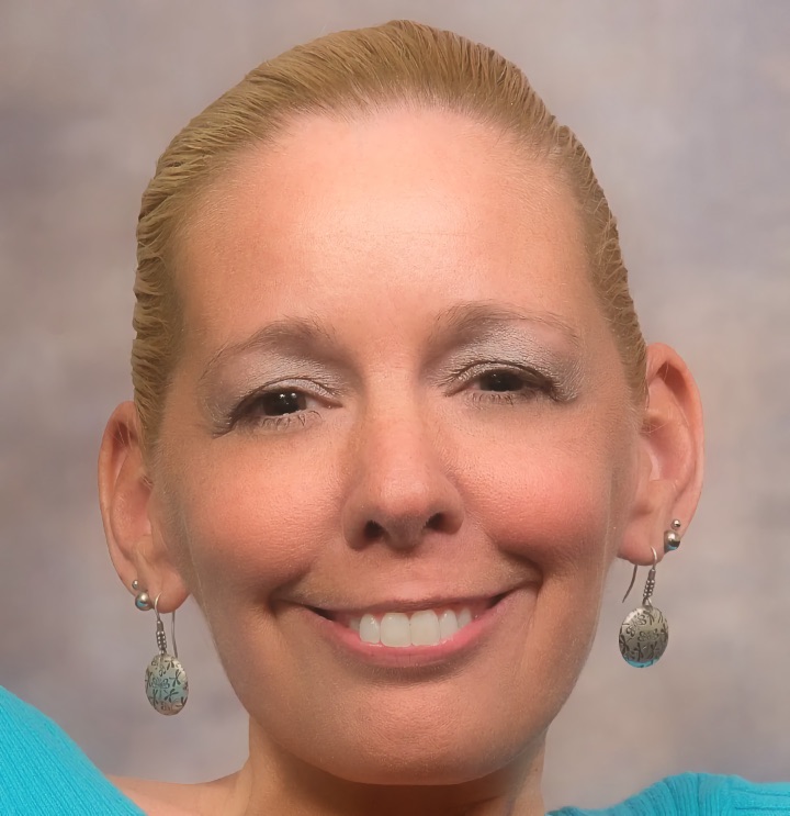An adult woman with light hair pulled back smiles at the camera in a studio portrait against a gray background.