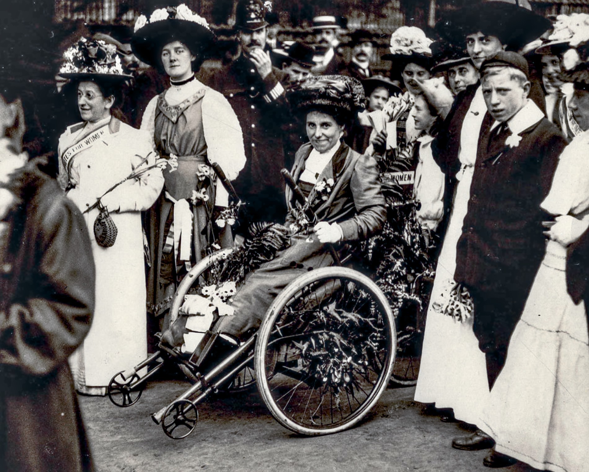 A woman uses a flower decorated hand operated tricycle at an outdoor gathering, surrounded by women and a uniformed police officer.