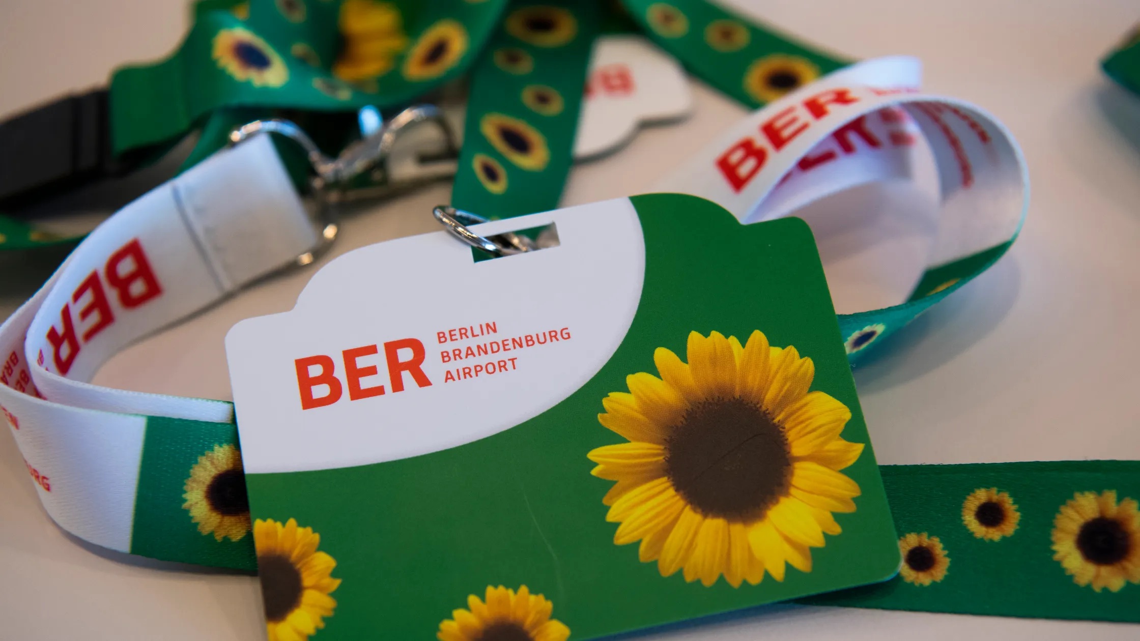 Close-up of green lanyards with a sunflower pattern and a BER Berlin Brandenburg Airport card resting on a table.