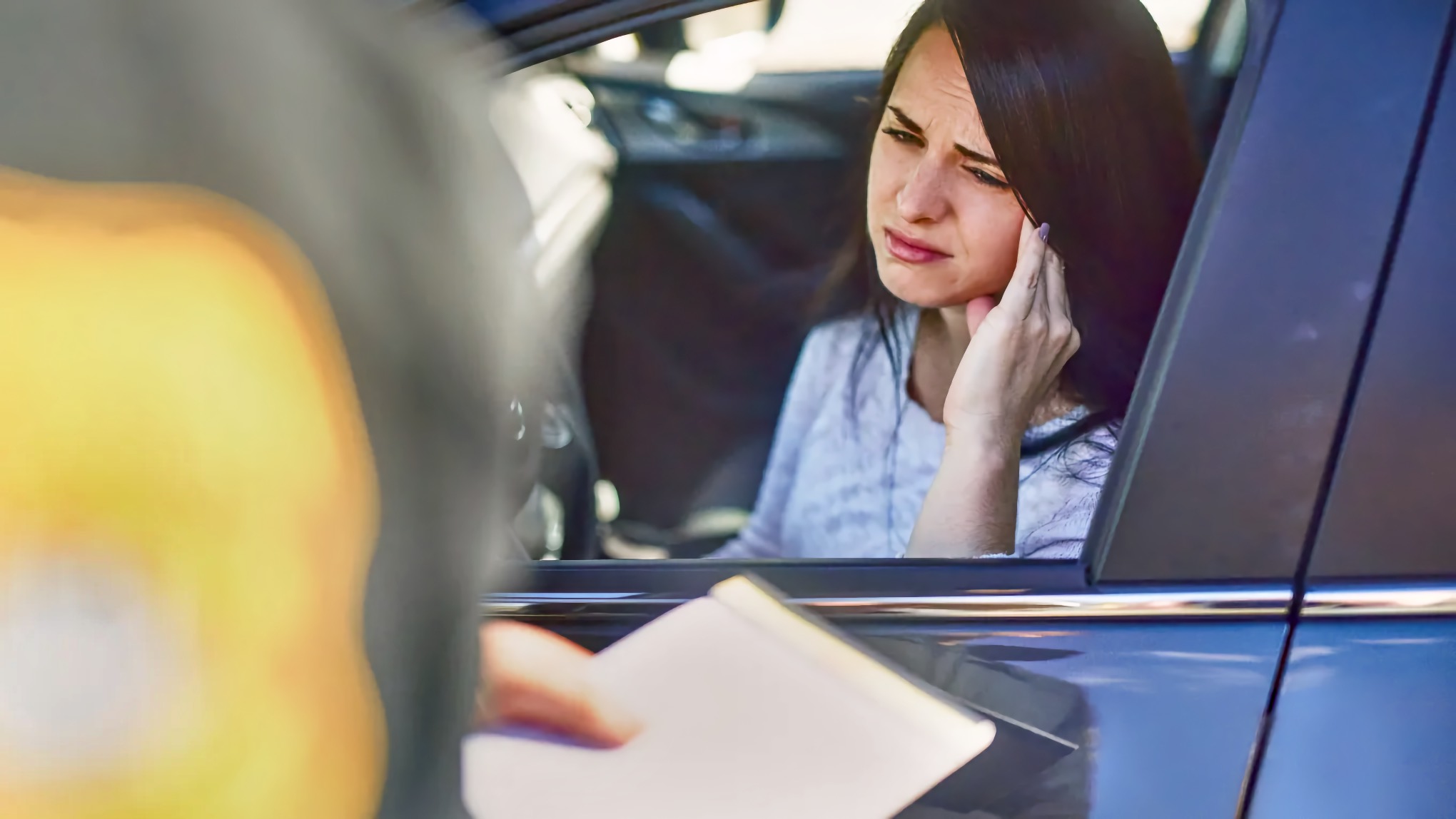 A woman with a distressed expression sits in a car during a traffic stop as a sheriff's deputy writes a citation at her window.