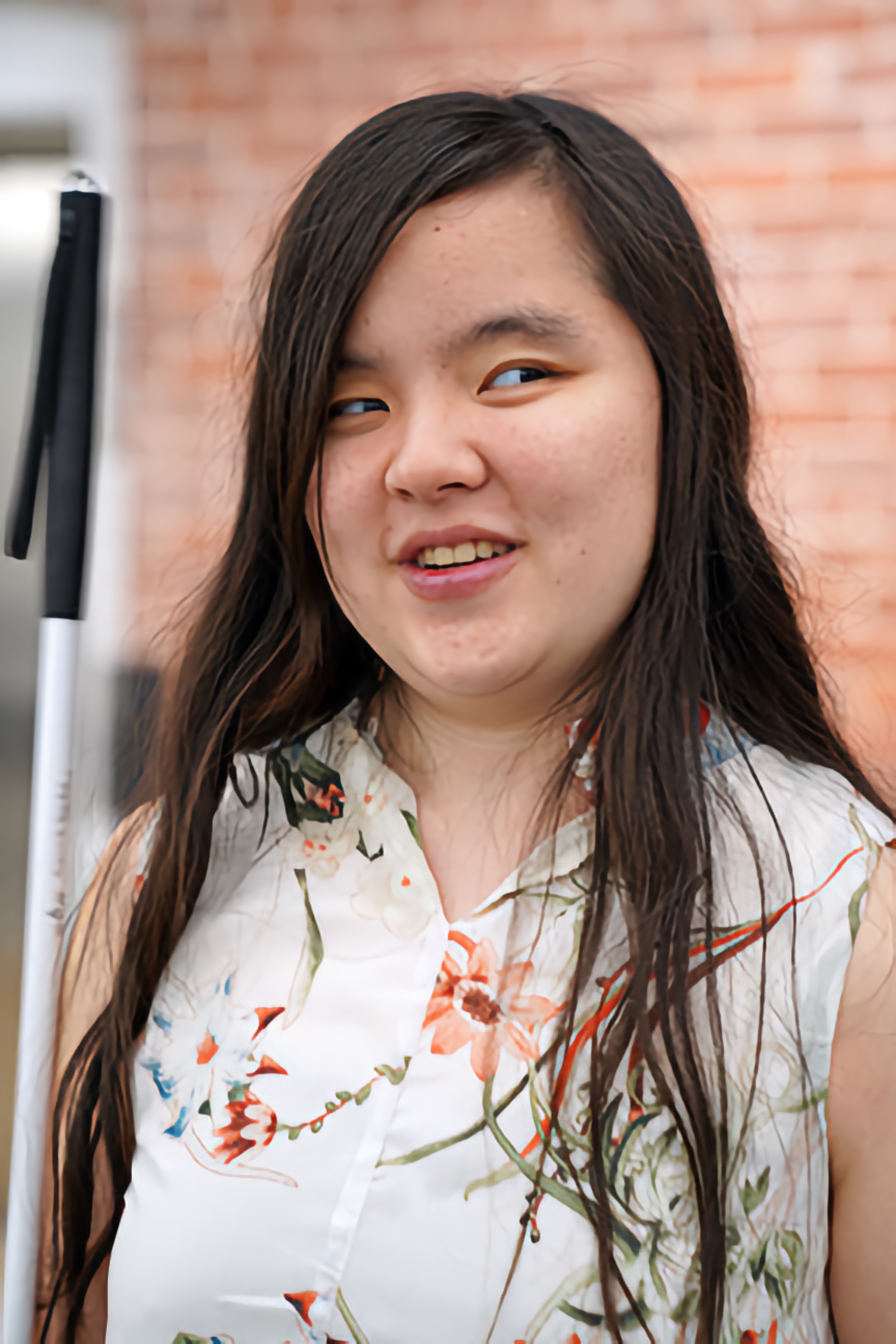 Cricket Bidleman, a young Blind woman, smiling brightly with her white cane by her side.