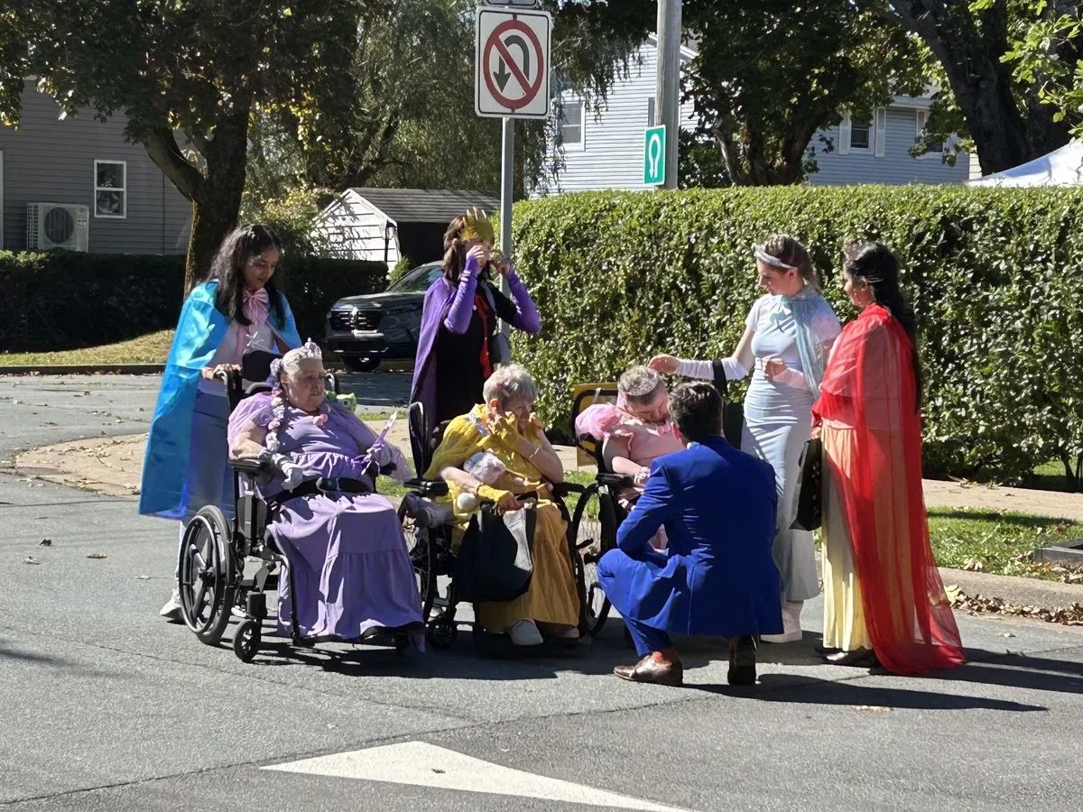 Costumed greeters at the Halifax Halloween Village Three people in wheelchairs, in costumes, are greeted on a sunny street by five costumed people who stand around them, one kneeling.
