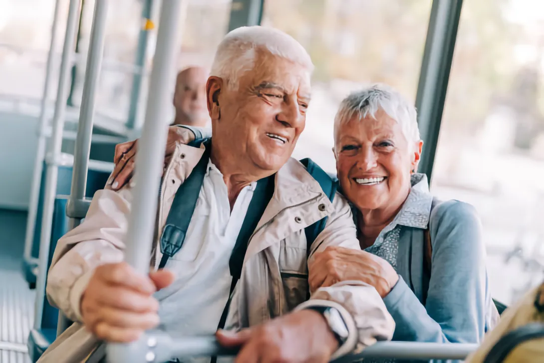 Older couple smile while seated together on Public Transportation.